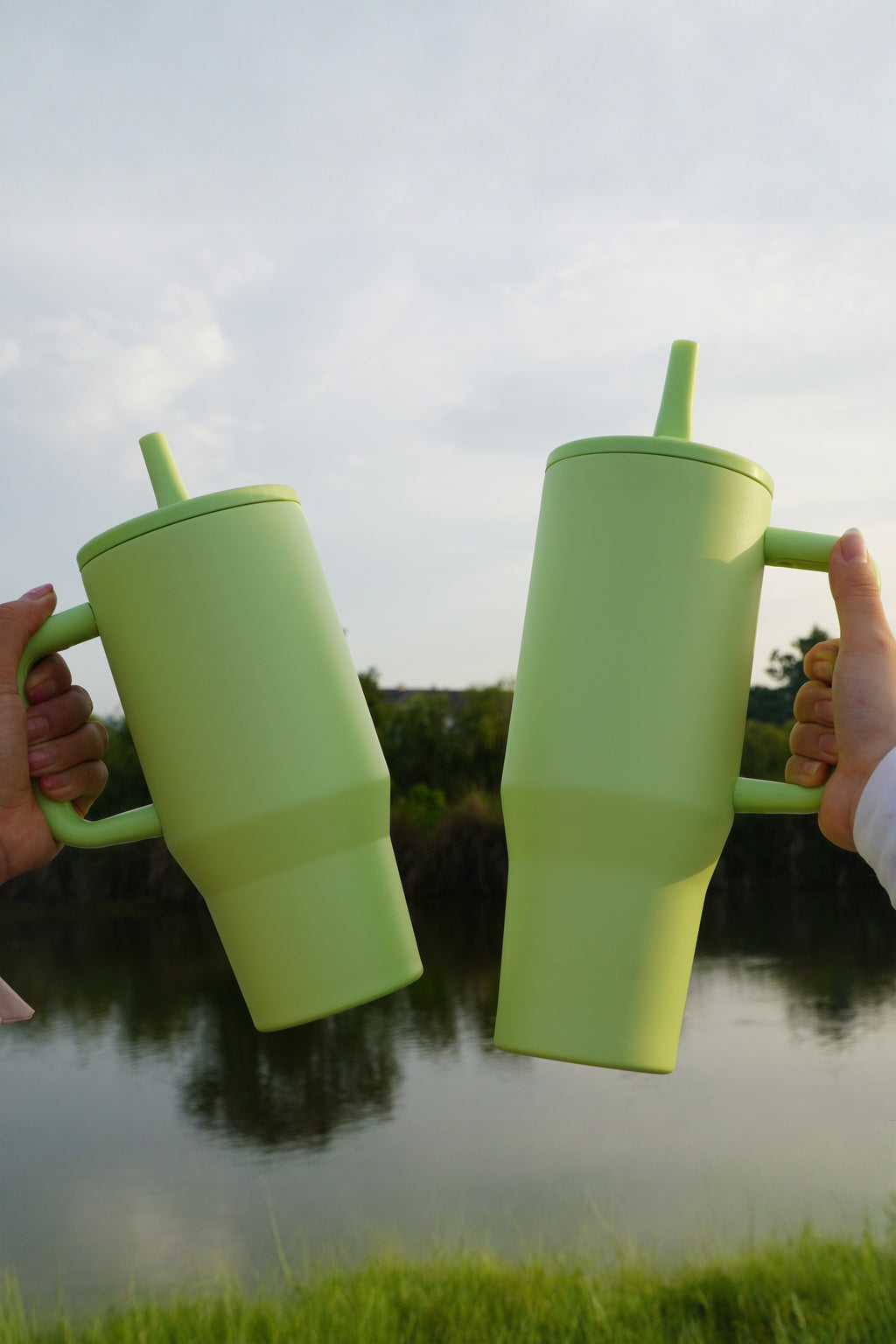 Two green 40oz tumblers held up by their handles, showing the size in the hand
