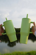 Two green 40oz tumblers held up by their handles, showing the size in the hand