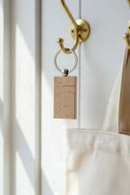 The beech rectangular keyring hanging from a brass hook beside a canvas tote bag