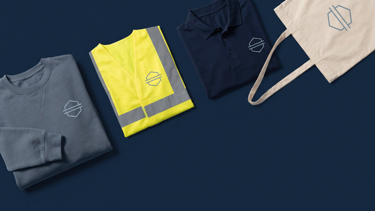 A flat-lay of workwear and merch - a hi-vis vest, a polo, a sweatshirt and a tote - each printed with the same emblem