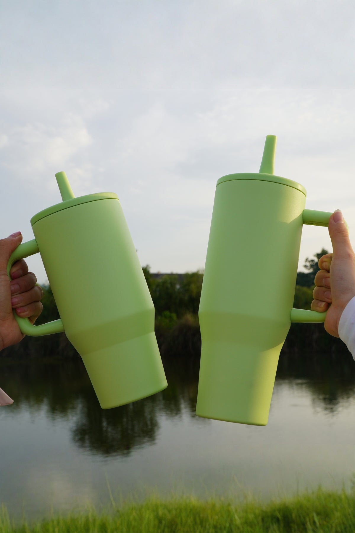Two green 40oz tumblers held up by their handles, showing the size in the hand