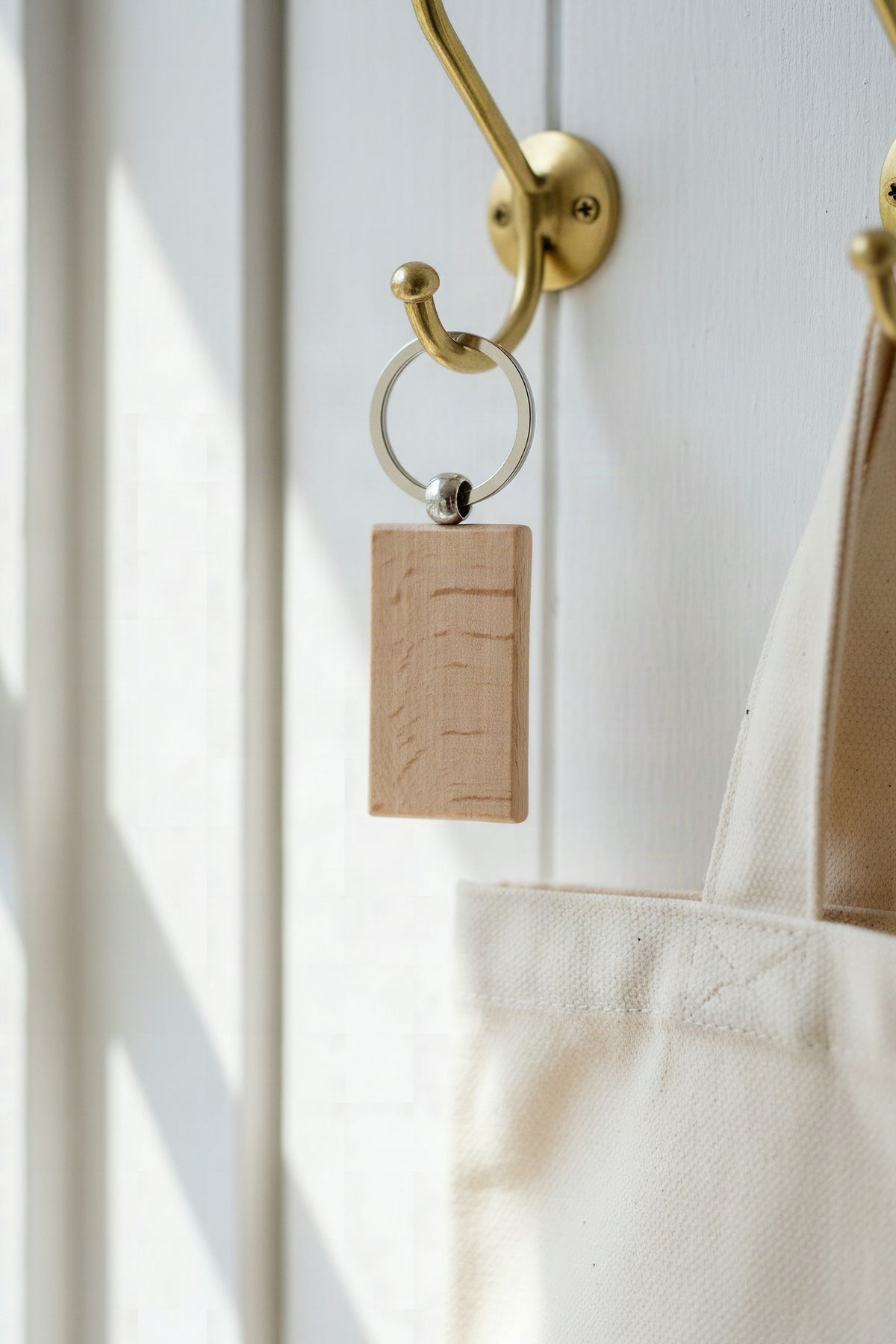 The beech rectangular keyring hanging from a brass hook beside a canvas tote bag