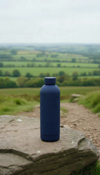 The navy bottle on a rock on a hillside path, green fields behind
