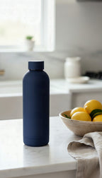 The navy bottle on a kitchen worktop beside a bowl of lemons