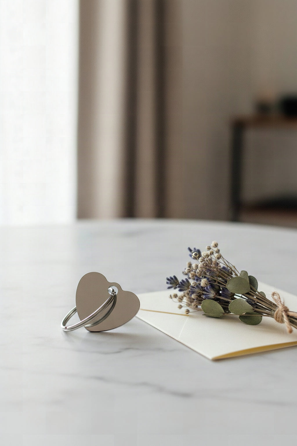 The steel heart keyring on marble beside dried flowers and a folded card