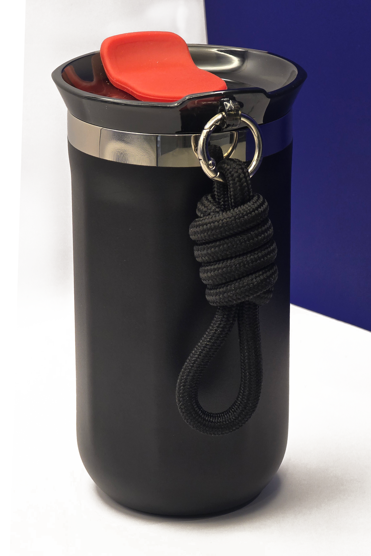 The top of the cup close up, showing the polished steel collar, the red flap on the lid and the knotted carry rope