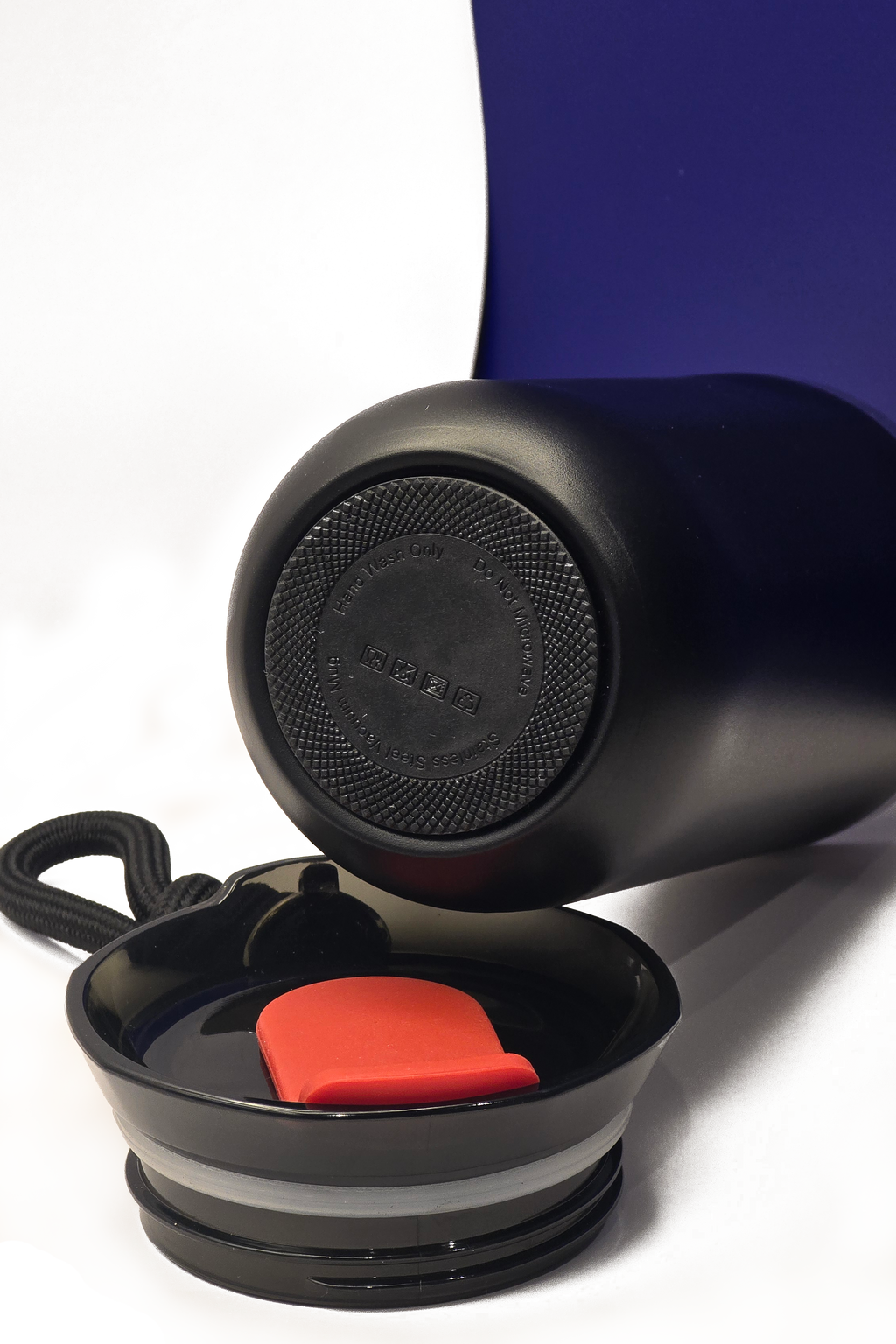 The cup on its side showing its grippy black base, with the lid lying open in front of it