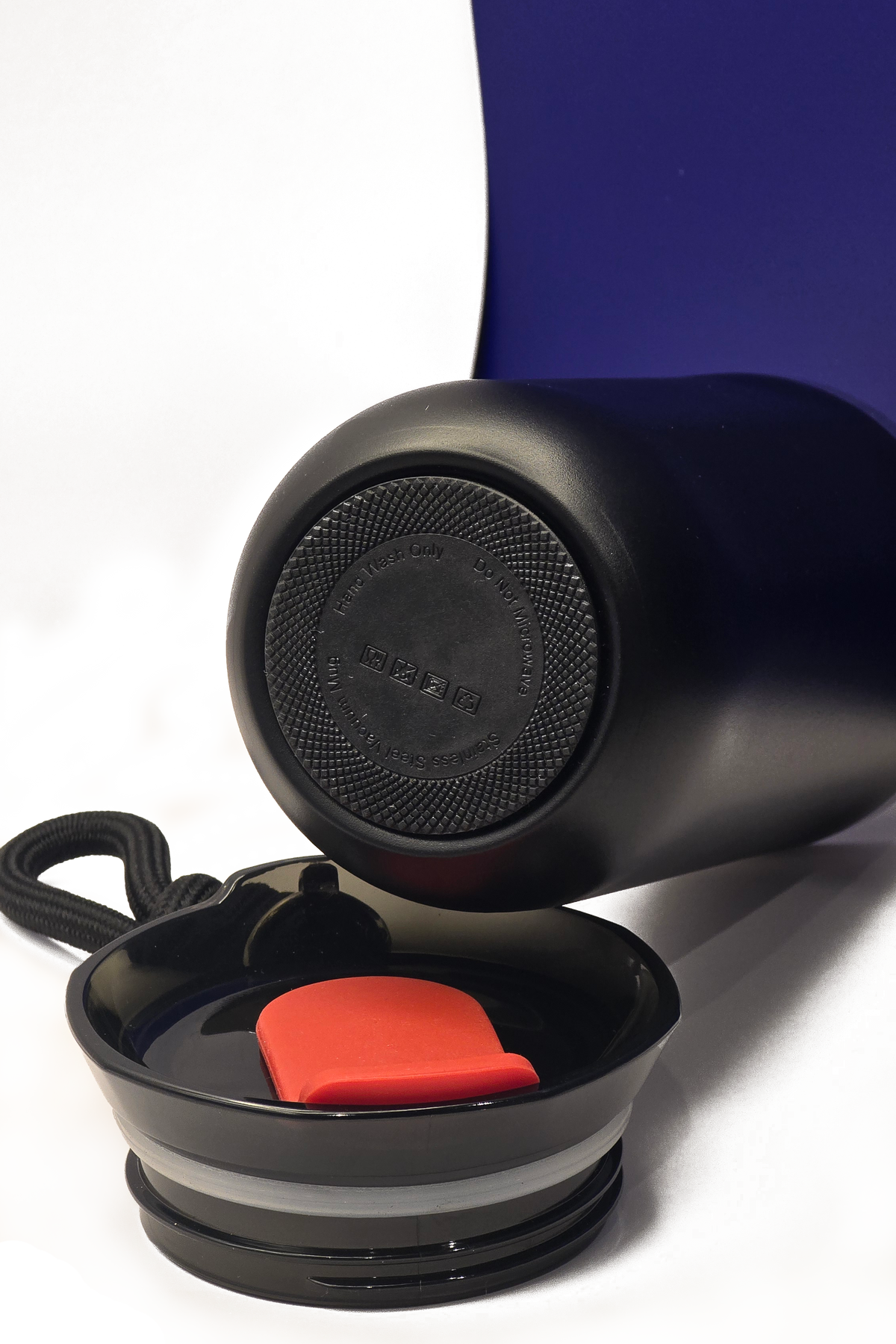 The cup on its side showing its grippy black base, with the lid lying open in front of it