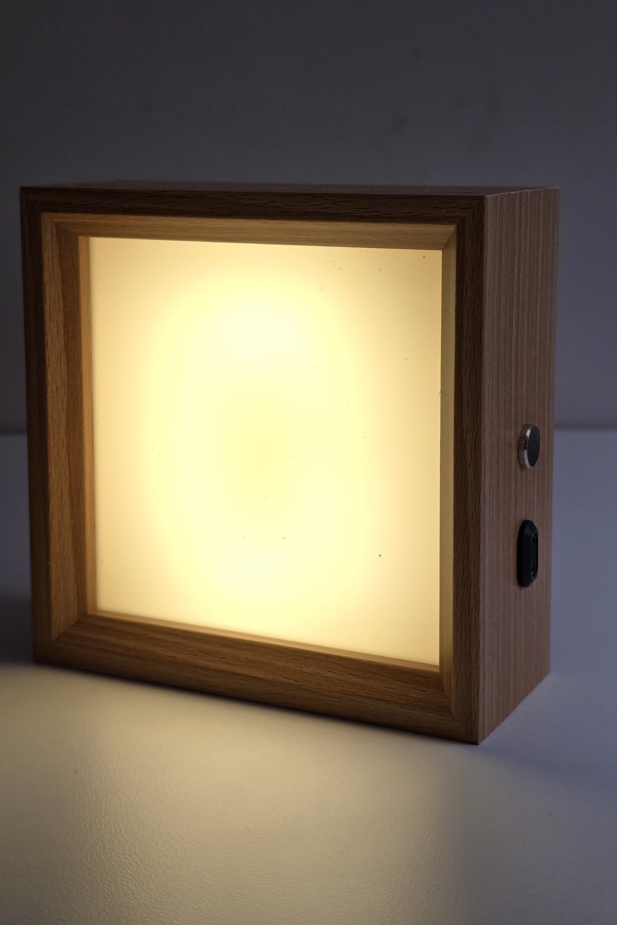 Square wooden photo night light lit in warm white, with the touch button and USB-C port on its side