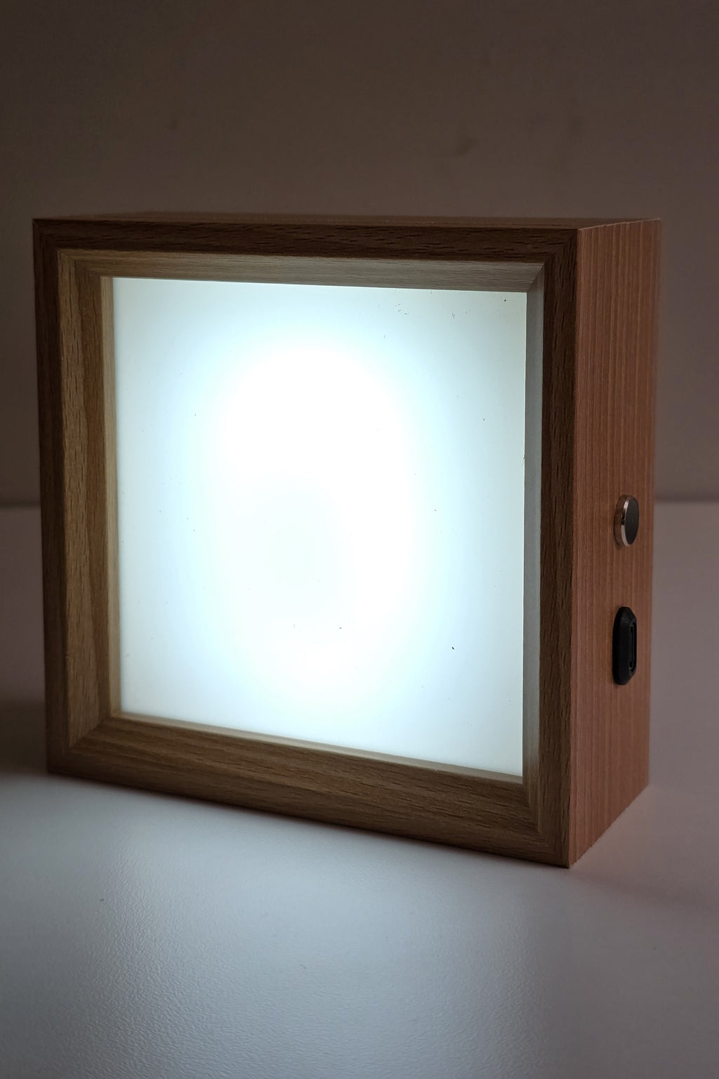 Square wooden photo night light lit in cool white, the frosted panel glowing evenly inside the wood frame