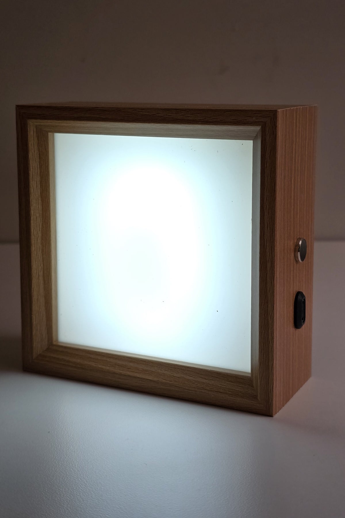 Square wooden photo night light lit in cool white, the frosted panel glowing evenly inside the wood frame